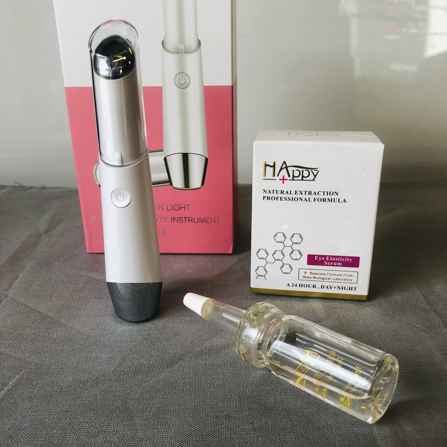 Valkoinen silmänympärysseerumipakkaus, lasinen seerumipullo ja valkoinen sähköinen silmänympäryshierontalaite.