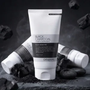 Kolme valko-mustaa DERMAL Black Charcoal Deep Cleanser 150 g -puhdistusvaahtotuobia tummalla kivipinnalla. Yksi tuubi seisoo pystyssä etualalla ja kaksi muuta makaa kyljellään sen takana sivuilla. Pakkausten juurella ja taustalla on puuhiilen paloja, hiilipölyä, tummia sileitä kiviä ja leijuvaa savua.