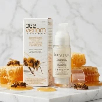 Diet Esthetic Bee Venom Essence kiinteyttävä ihoseerumi pumppupullossa ja tuotepakkaus marmoritasolla hunajakennojen, valuvan hunajan ja mehiläisten ympäröimänä.