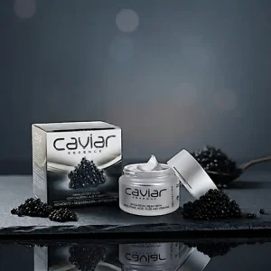 Diet Esthetic Caviar Essence -kaviaarivoide avatussa huurrelasipurkissa ja sen kiiltävä hopeamusta pakkaus tummalla liuskekivialustalla, ympäröitynä mustilla kaviaarihelmillä.