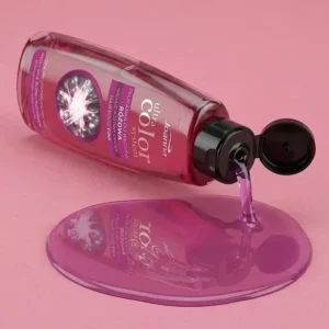 Vaaleanpunainen Joanna Ultra Color -hiushuuhtelupullo kallellaan, josta valuu kirkasta pinkkiä nestettä siistiksi lammikoksi pehmeälle vaaleanpunaiselle taustalle.