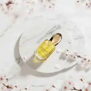 Lasipullo täynnä kultaista Mercilen Moon God Flower -kasvoöljyä ja musta pakkaus, jota koristaa näyttävä valkoinen kukka.