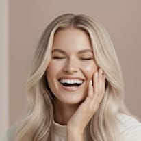 Naurava nainen, jolla on kuulas ja hoidettu iho sekä vaaleat laineikkaat hiukset.