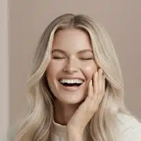 Naurava nainen, jolla on kuulas ja hoidettu iho sekä vaaleat laineikkaat hiukset.