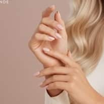 Lähikuva huolitelluista käsistä, joissa on kauniit nuden sävyiset kynnet ja vaaleanpunainen tausta.