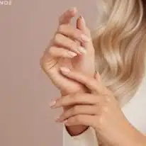 Lähikuva huolitelluista käsistä, joissa on kauniit nuden sävyiset kynnet ja vaaleanpunainen tausta.