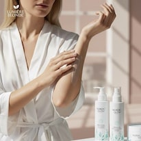 Nainen levittää voidetta käsivarteen, vieressä Nordic Glow -vartalonhoitotuotteita valkoisissa pulloissa.