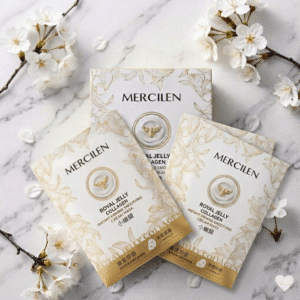 Mercilen Royal Jelly Collagen -kasvonaamiopakkaus ja kaksi yksittäispakattua naamiopussia aseteltuna valkoiselle marmorille, jota ympäröivät vaaleat kirsikankukan oksat.