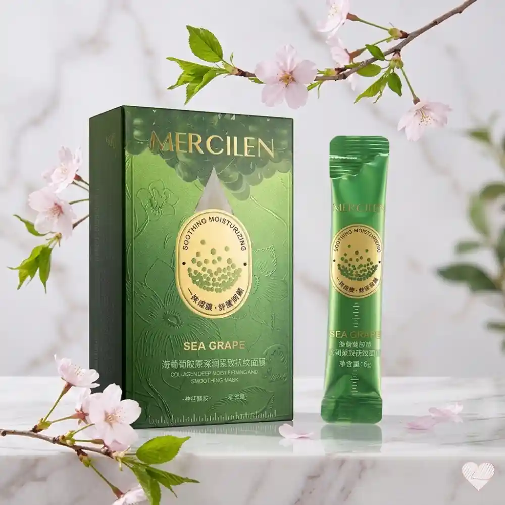 Smaragdinvihreä Mercilen Sea Grape Collagen -tuotepakkaus ja yksittäinen kapea annospussi aseteltuna vaalealle marmorialustalle vaaleanpunaisten kirsikankukkien ja vihreiden lehden ympäröimänä.