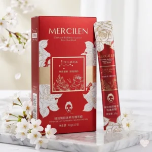 Ylellinen punainen Mercilen Rose Tea Mask -pakkaus ja kapea annospussi aseteltuna marmorialustalle valkoisten kirsikankukkien keskelle.