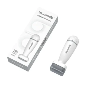 Viistosti aseteltu valkoinen Bio Needle säädettävä derma stamp -mikroneulauslaite suojakorkilla sekä sen vieressä lappeellaan lepäävä vaalea myyntipakkaus valkoisella taustalla. Pakkauksen etupuolella on brändilogo ja tuotekuva, ja itse laitteessa on näkyvillä harmaa numeroitu pituudensäätökiekko.