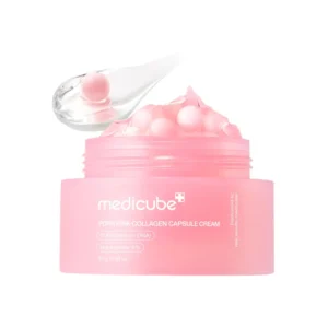 Avattu vaaleanpunainen Medicube PDRN Pink Collagen Capsule Cream -voidepurkki ja sen yläpuolella leijuva läpinäkyvä spaatteli, jossa on kirkasta geeliä ja yksittäinen vaaleanpunainen kollageenikapseli puhtaalla valkoisella taustalla.