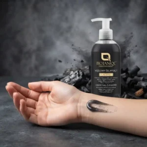 Sively tummaa Biotaniqe Pure Detox Charcoal Cleanser -aktiivihiiligeeliä ranteella, taustalla puhdistusgeelipullo ja puuhiilen palasia usvaisella taustalla.