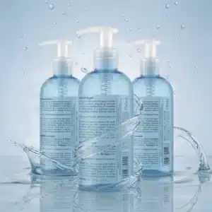 Kolme vaaleansinistä Biotaniqe Gentle Foaming Face Cleanser -kasvojenpuhdistusvaahdon 250 ml pumppupulloa takaapäin ryhmässä veden pinnalla, etualalla pyörivä raikas vesiroiske ja kimaltelevia vesipisaroita.