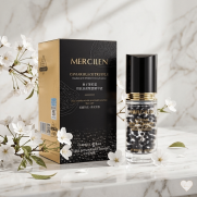 Mercilen Caviar Black Truffle -seerumipullo, joka sisältää mustia helmiäisiä kapseleita, ja musta-kultainen myyntipakkaus marmorialustalla valkoisten kirsikankukkien ympäröimänä.