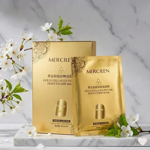 Kultainen Mercilen Gold Collagen Peptide Honeycomb Mask -myyntipakkaus ja yksi naamiopussi aseteltuna valkoiselle marmorialustalle, jota ympäröivät kukkivat kirsikkapuun oksat.