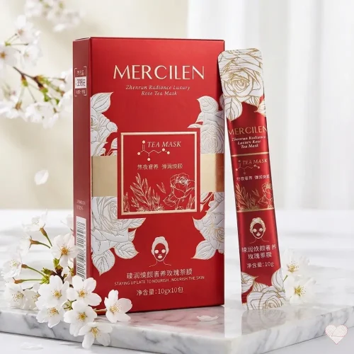 Ylellinen punainen Mercilen Rose Tea Mask -pakkaus ja kapea annospussi aseteltuna marmorialustalle valkoisten kirsikankukkien keskelle.